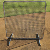 A baseball screen lying flat on the ground in a field, used for training or practice purposes.